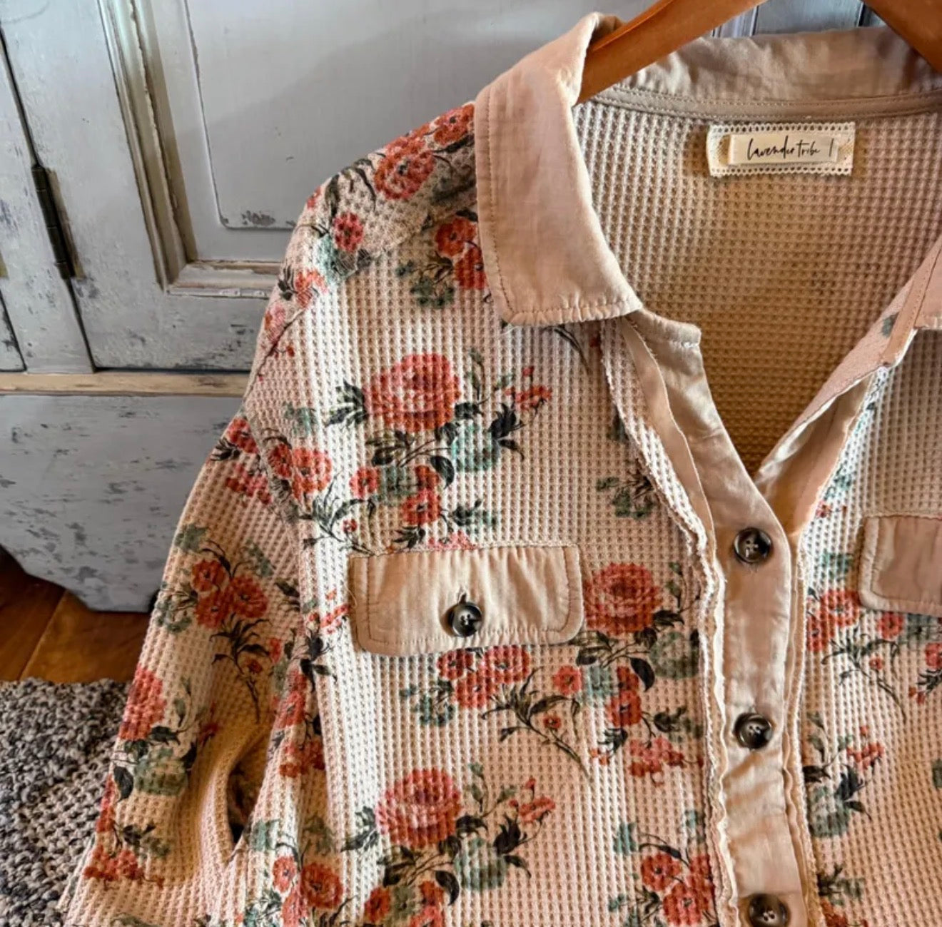 Floral patterned shirt with a textured vest over it, hanging on a wooden hanger.