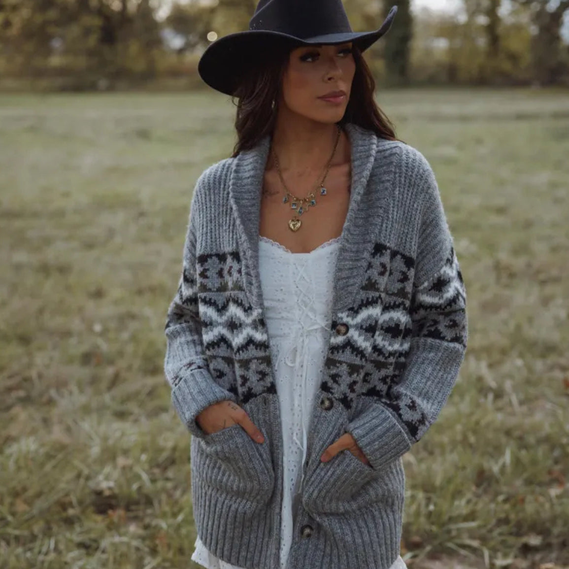 Woman wearing a patterned gray cardigan and black hat in a field