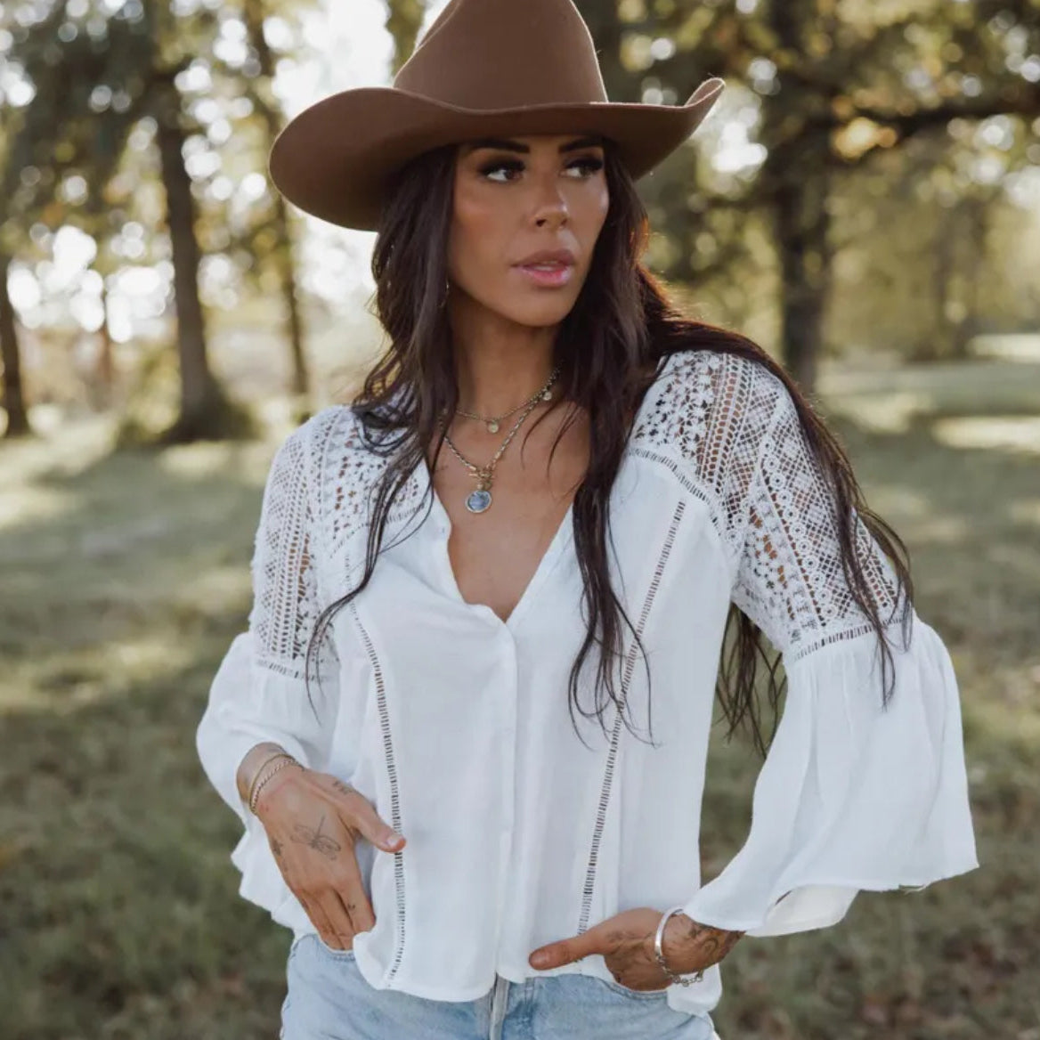Woman wearing a white lace blouse and brown hat outdoors