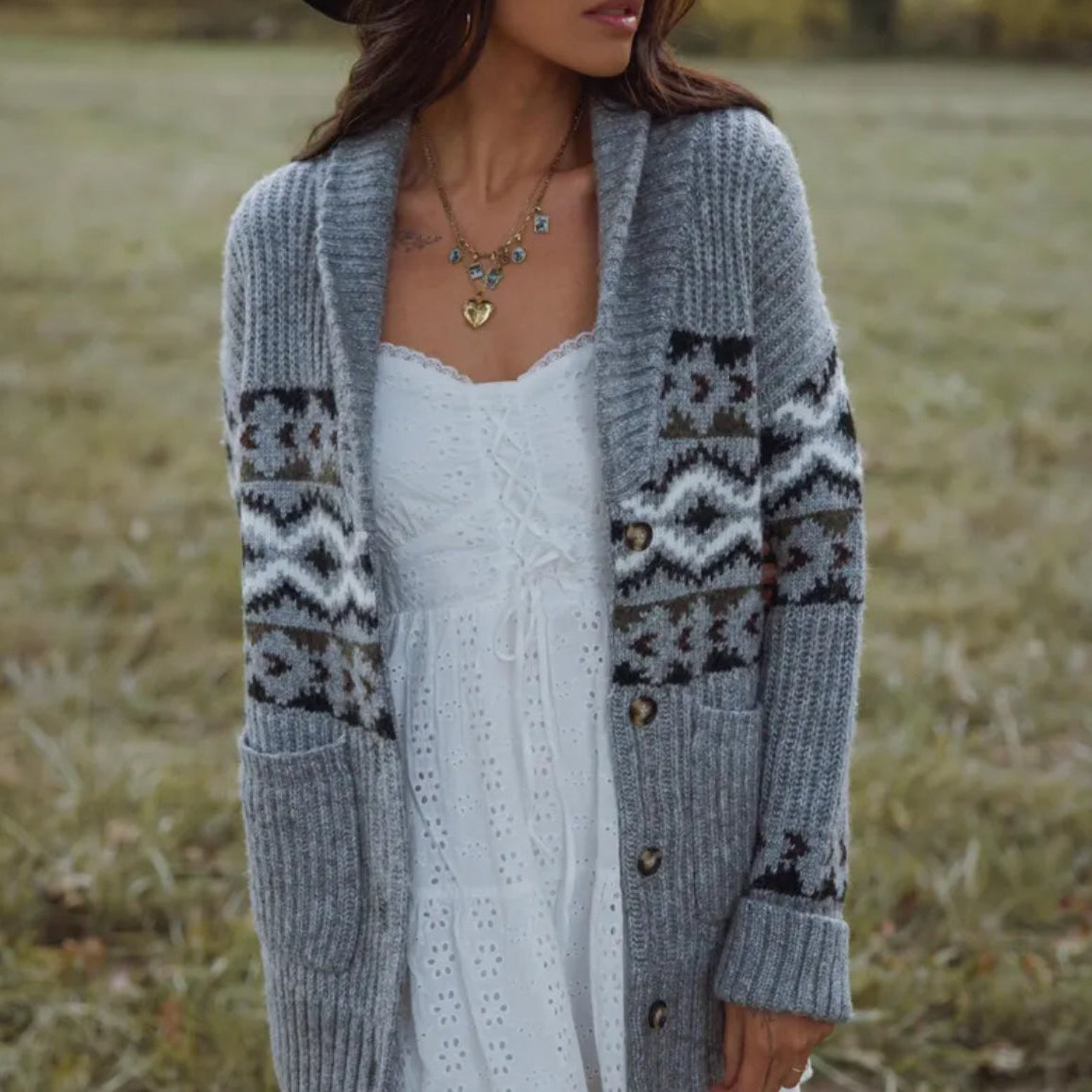 Woman wearing a patterned gray cardigan over a white dress in a field