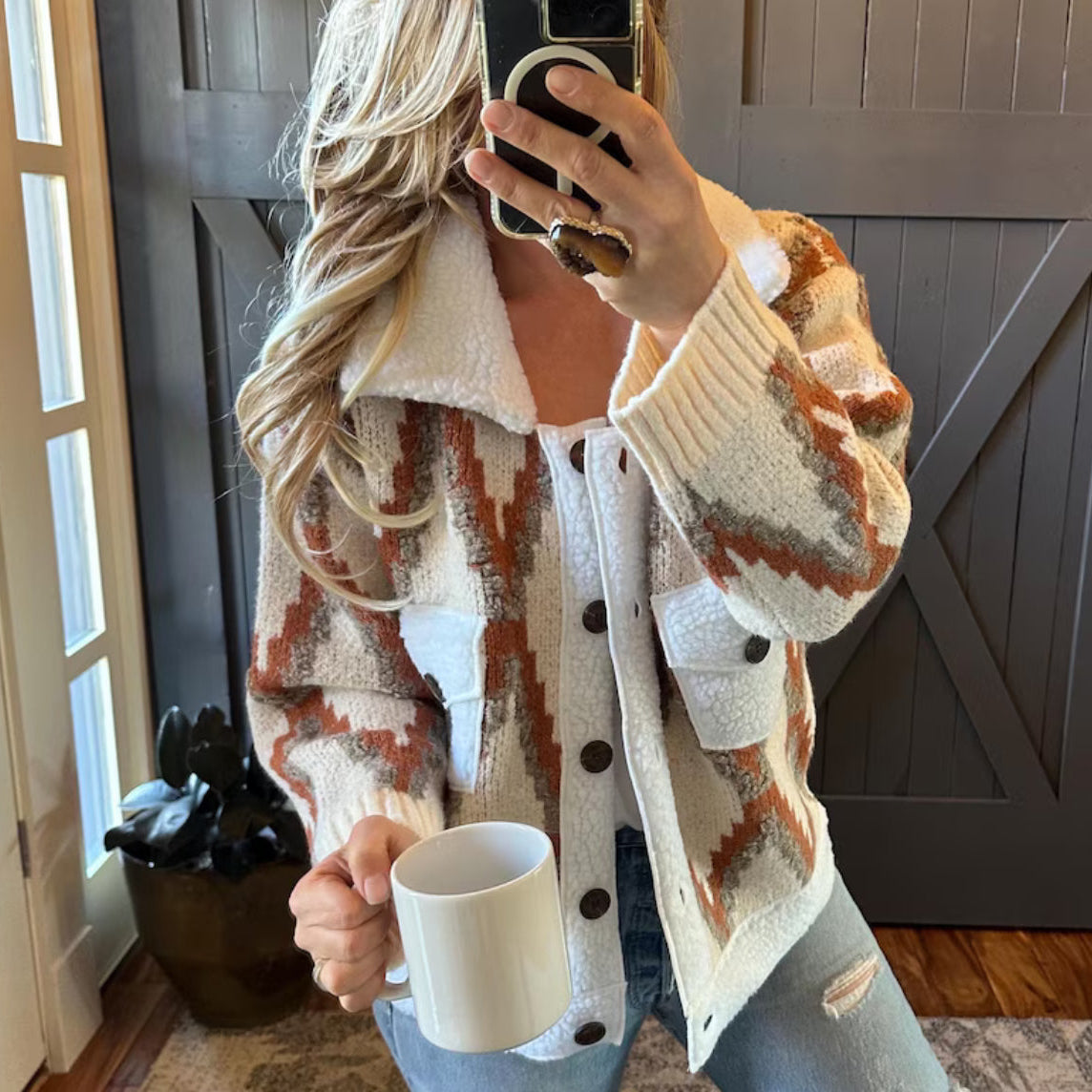 Person wearing a patterned cardigan holding a mug indoors.