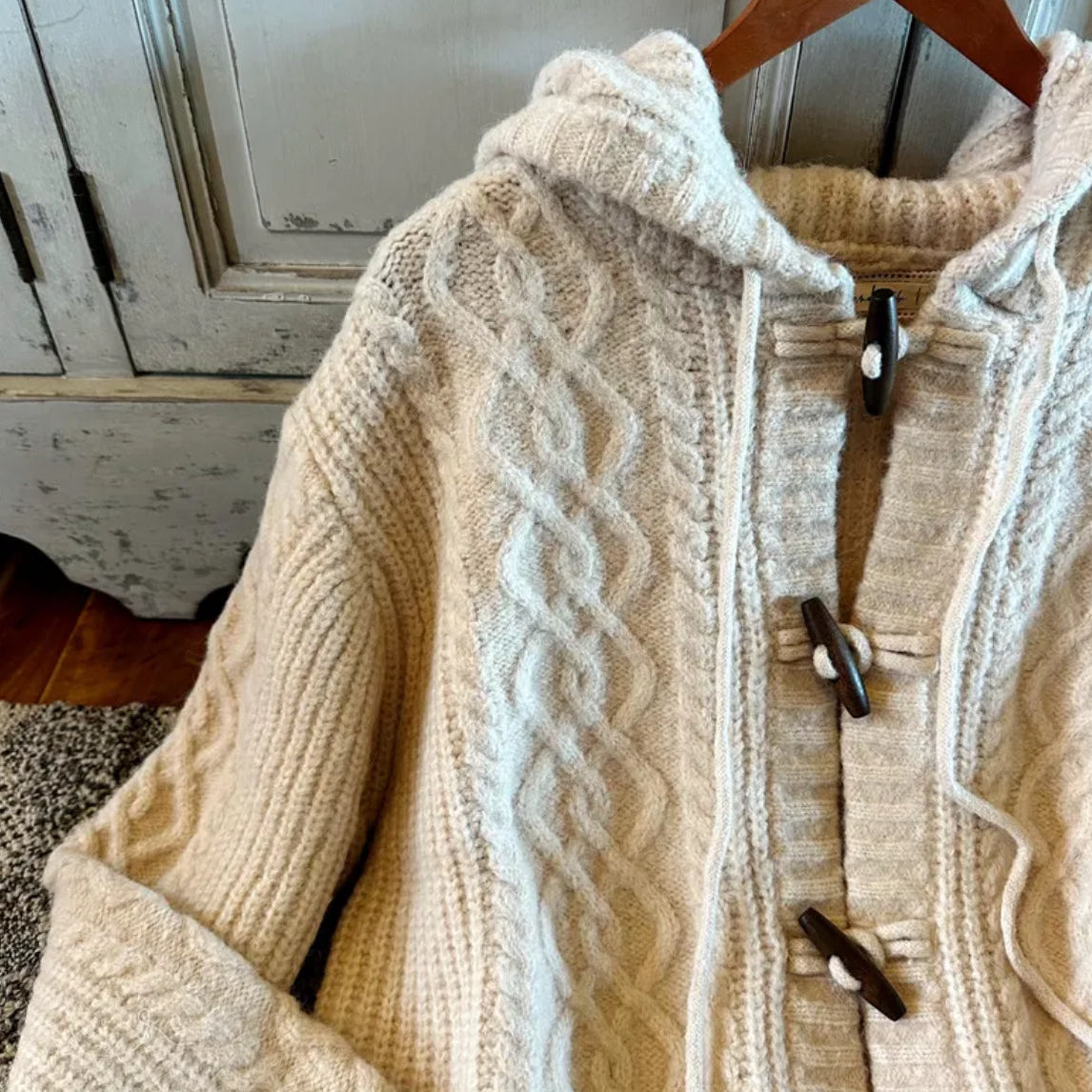 Beige cable knit sweater on a hanger with a rustic background