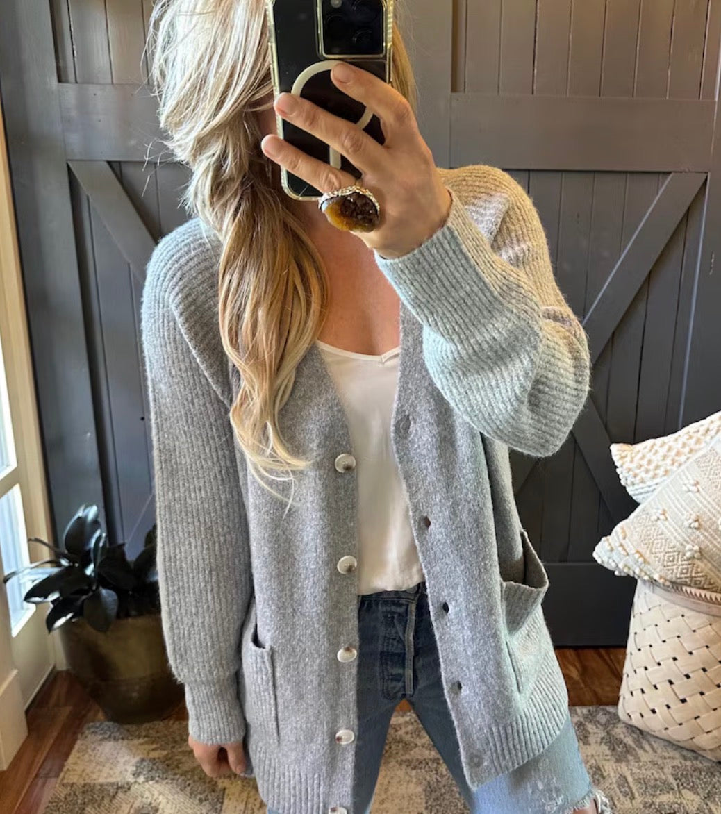 Person wearing a gray cardigan taking a mirror selfie in a home setting.