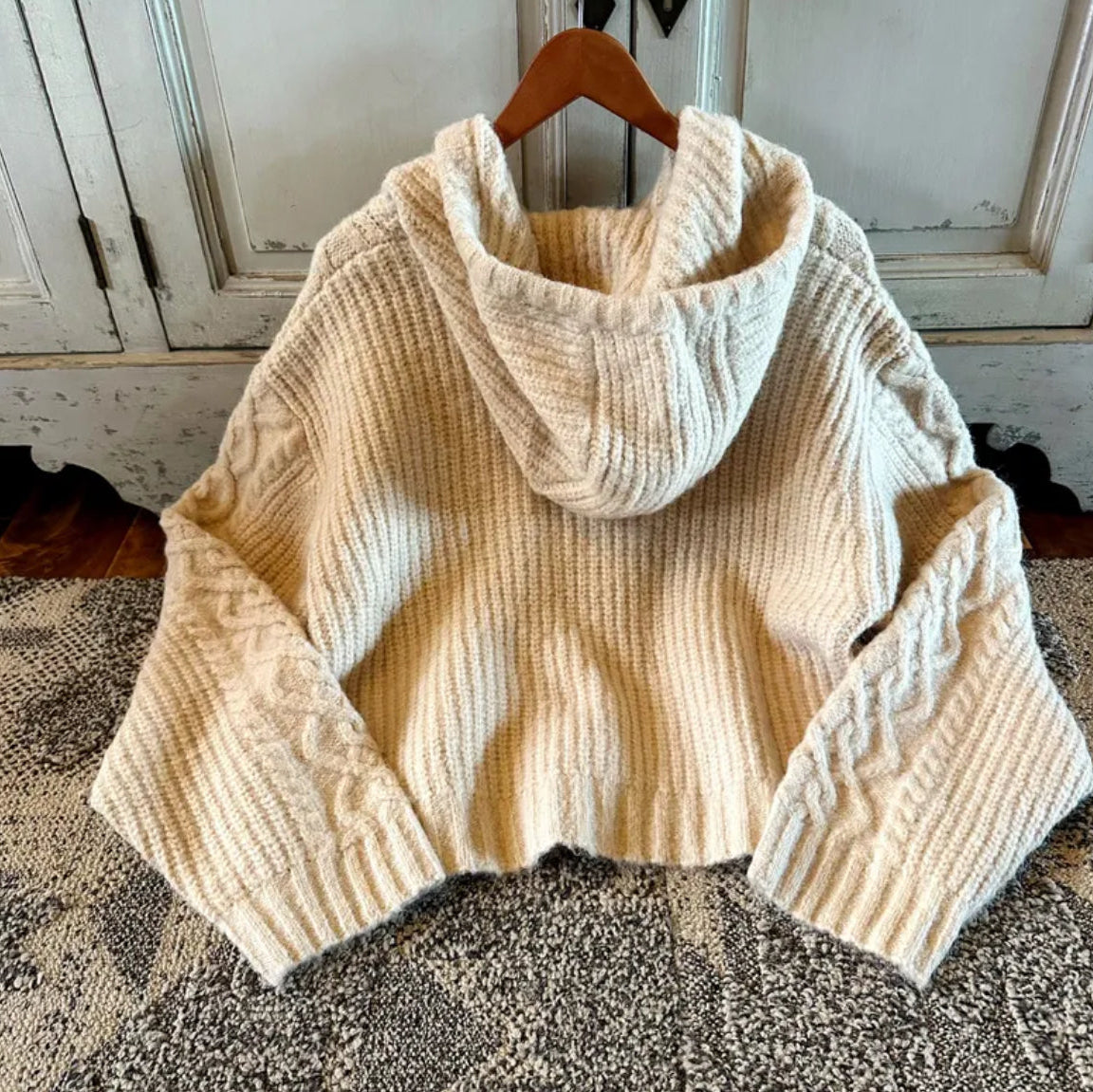 Beige knitted sweater on a wooden hanger against a neutral background
