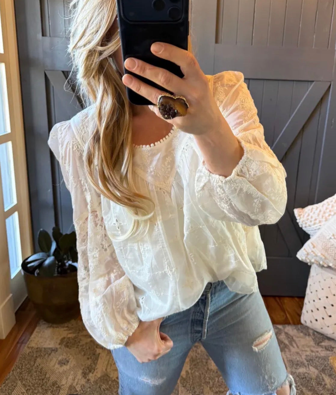 Person wearing a white lace top and blue jeans taking a mirror selfie.