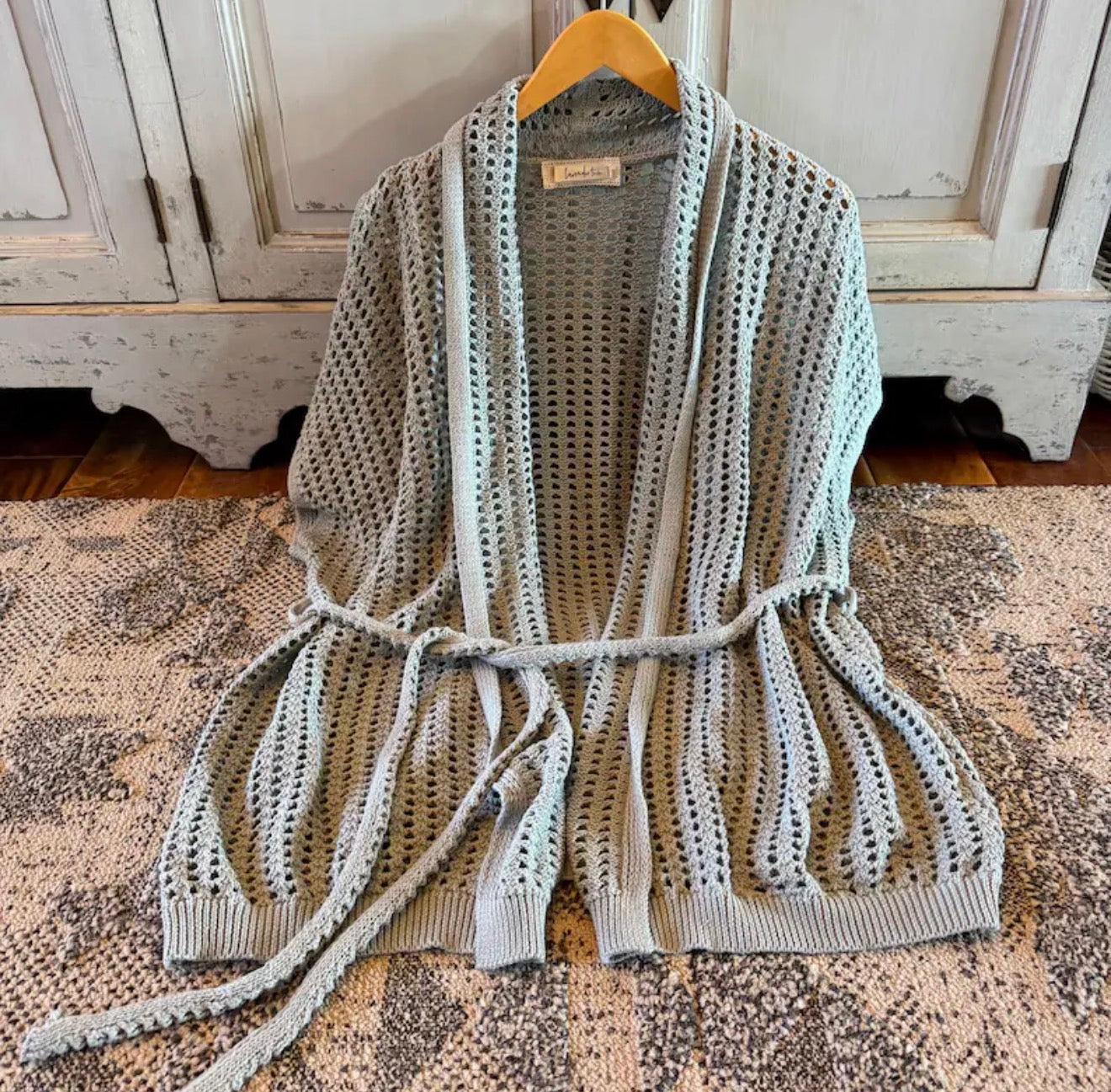 Knitted cardigan with a belt on a hanger against a rustic wooden cabinet background