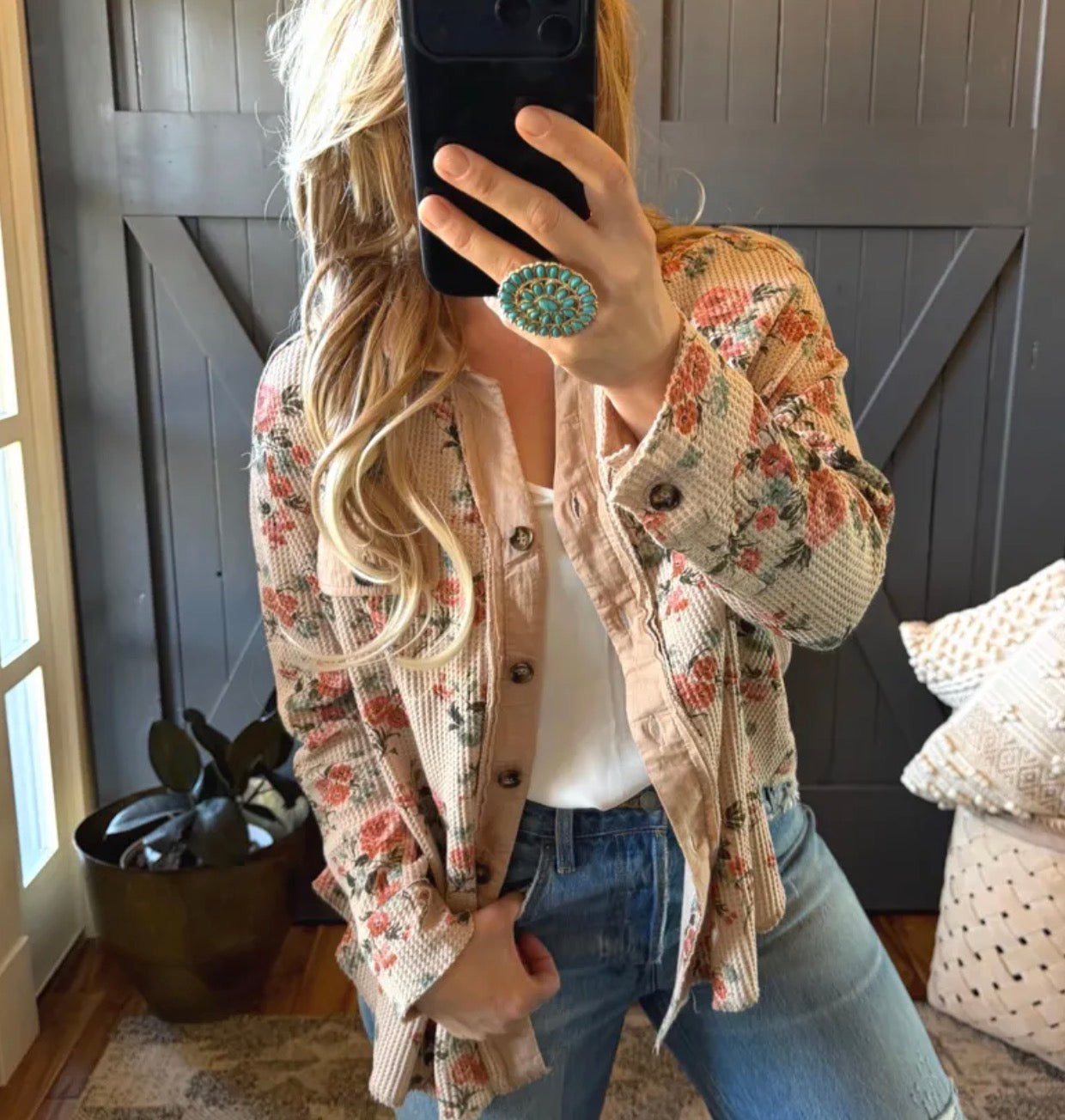 Person wearing a floral jacket and blue jeans taking a mirror selfie.