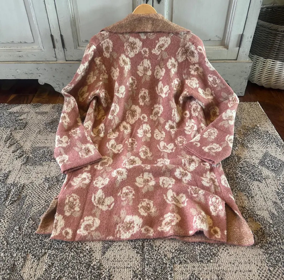 Pink floral-patterned coat on a wooden hanger against a neutral background