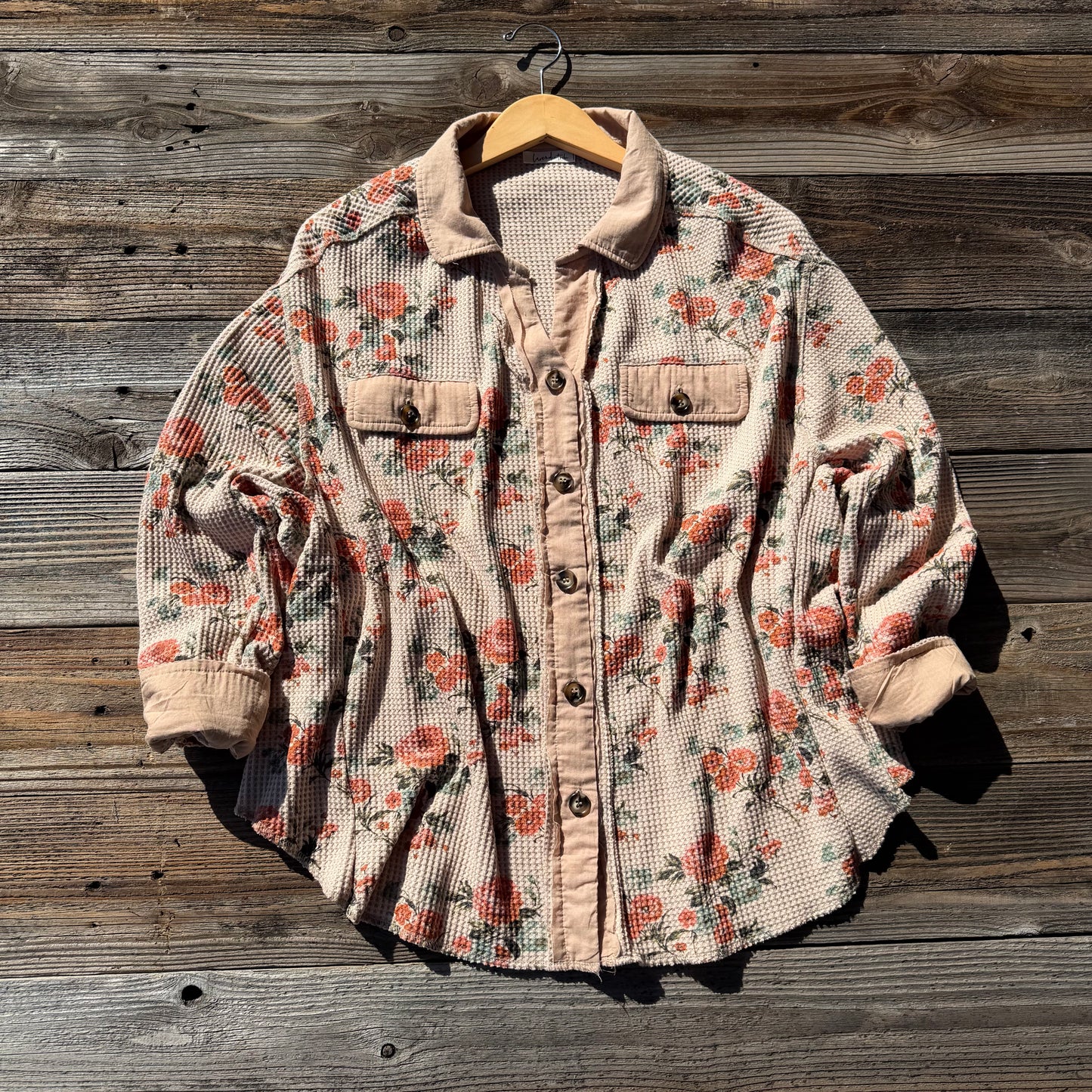 Floral patterned jacket on a wooden hanger against a wooden background