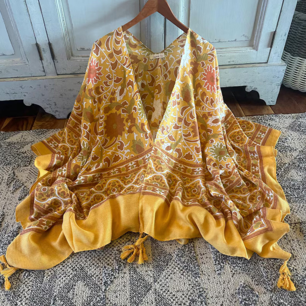 Yellow patterned scarf draped over a wooden hanger on a textured surface.