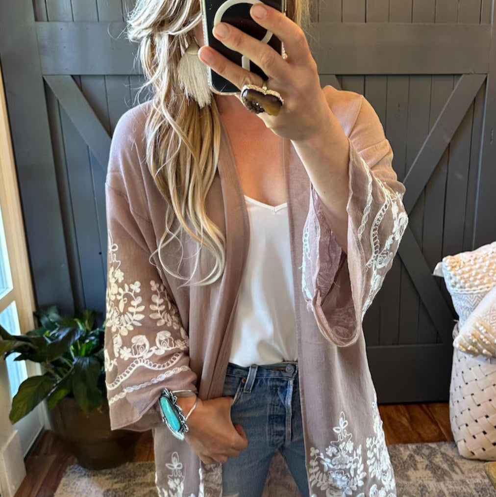 Woman wearing a light pink cardigan with lace details in a home setting.
