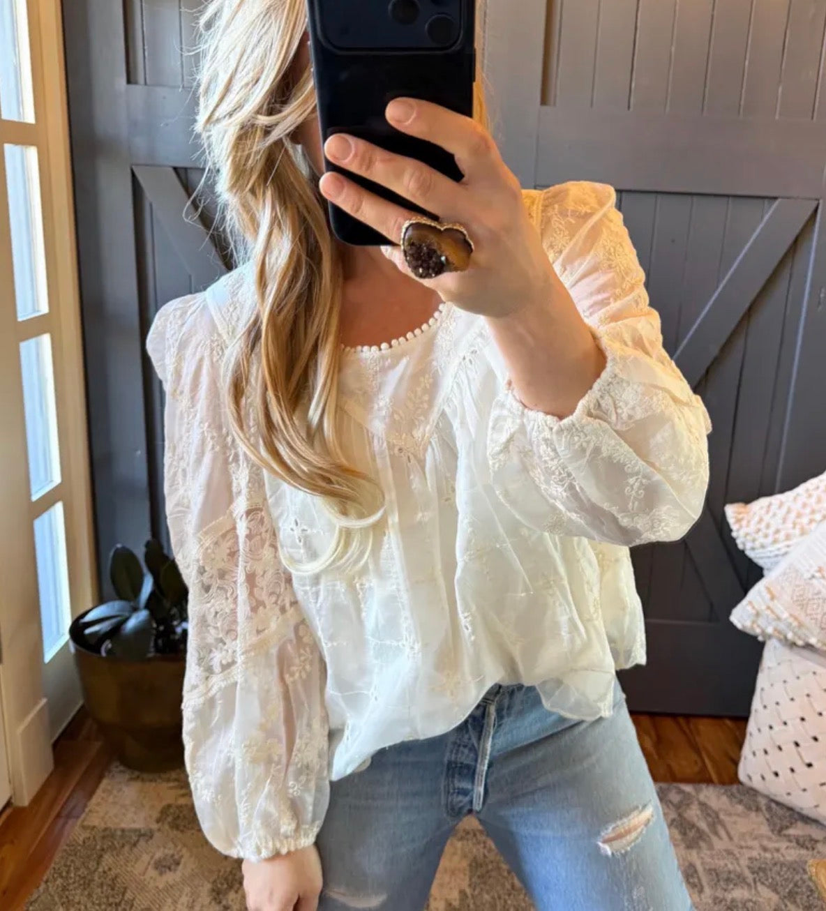 Person wearing a white lace top and jeans, taking a mirror selfie.