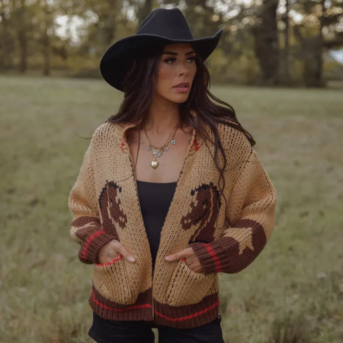 Woman wearing a patterned cardigan and hat in a field