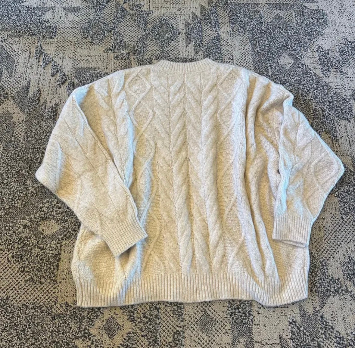 Beige cable knit sweater on a textured surface