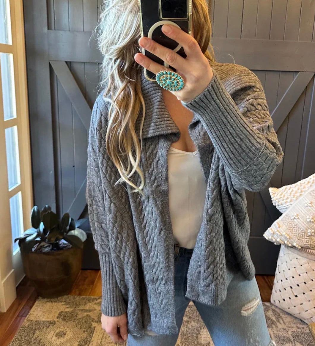 Person wearing a gray cable knit cardigan taking a mirror selfie.
