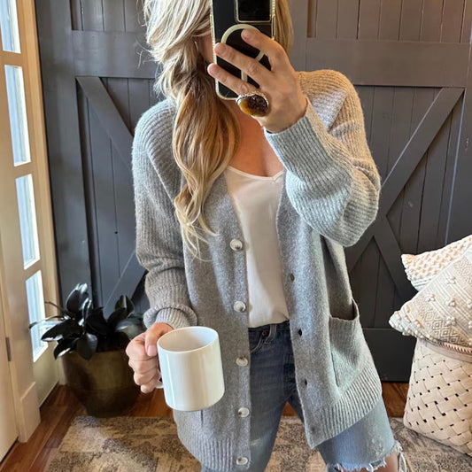 Person wearing a gray cardigan and holding a white mug indoors.