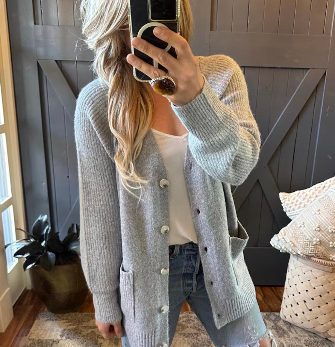 Person wearing a gray cardigan with white buttons in a home setting.