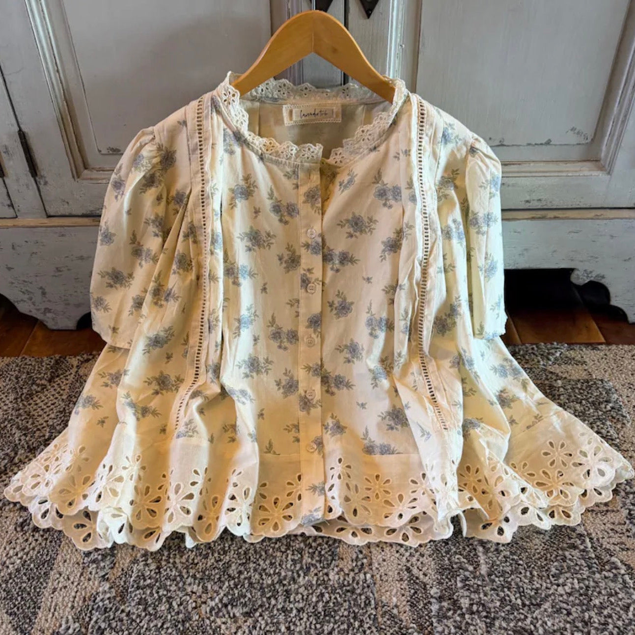 Floral lace blouse on a hanger against a neutral background