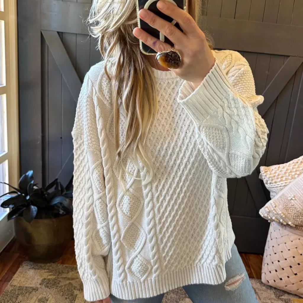 Person wearing a white cable knit sweater taking a mirror selfie.