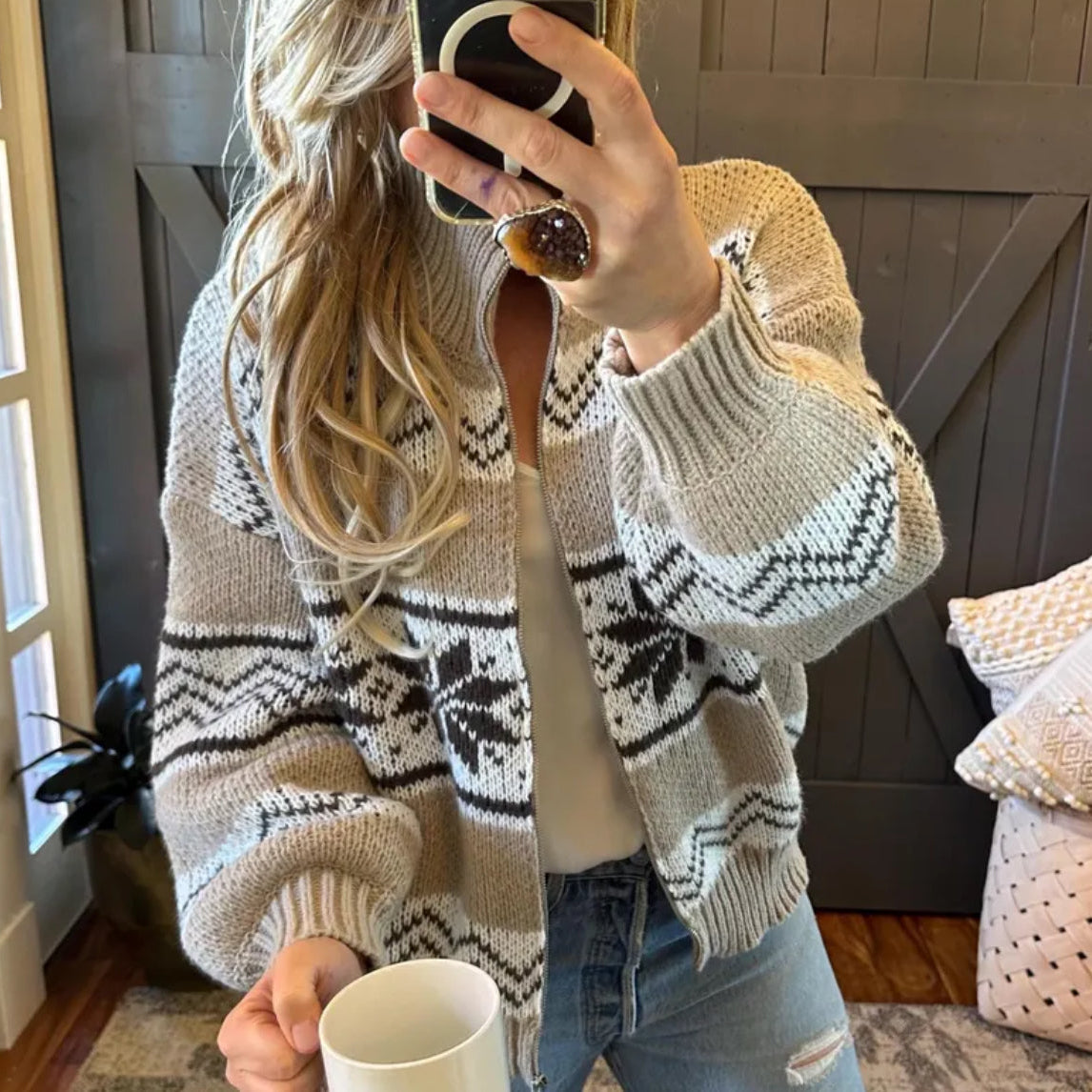 Person wearing a patterned cardigan holding a cup indoors.