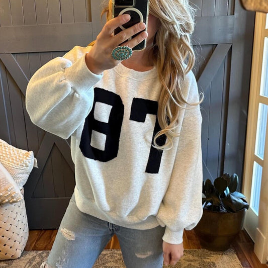 Person wearing a white sweatshirt with large black numbers, taking a mirror selfie.