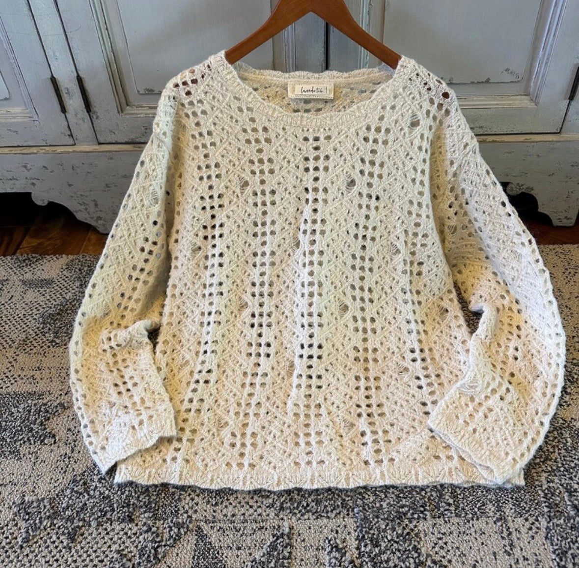 Beige crochet sweater on a wooden hanger against a rustic background