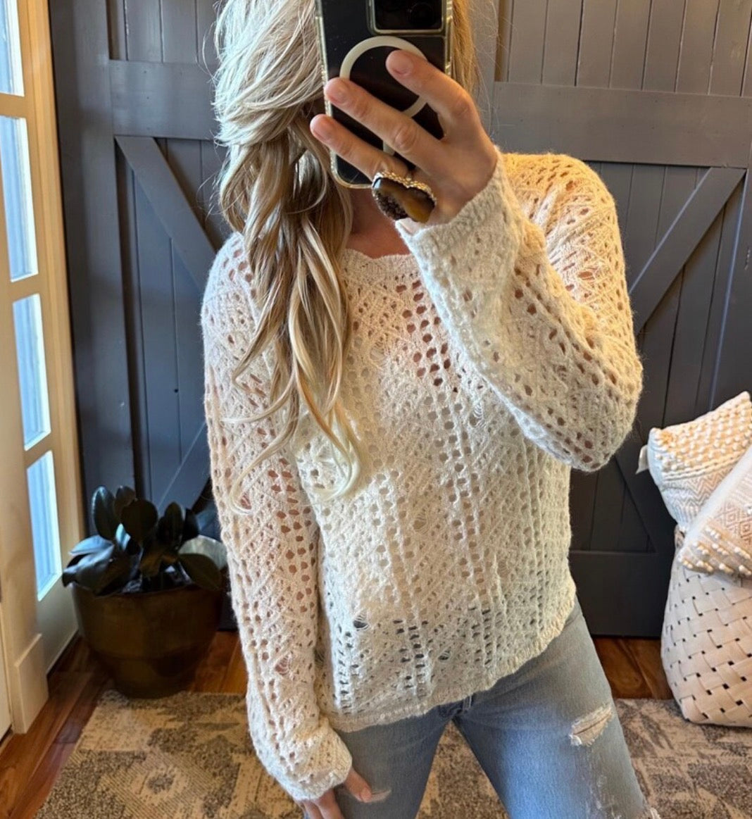 Person wearing a beige crochet sweater taking a mirror selfie.