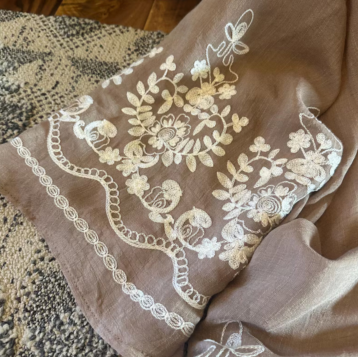 Brown fabric with white floral embroidery on a textured surface