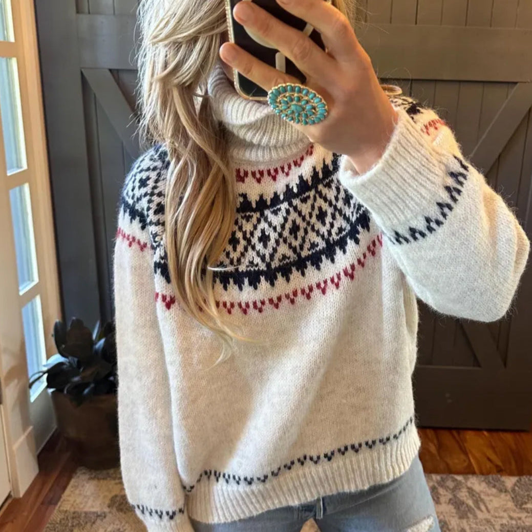 Person wearing a patterned sweater taking a mirror selfie indoors.