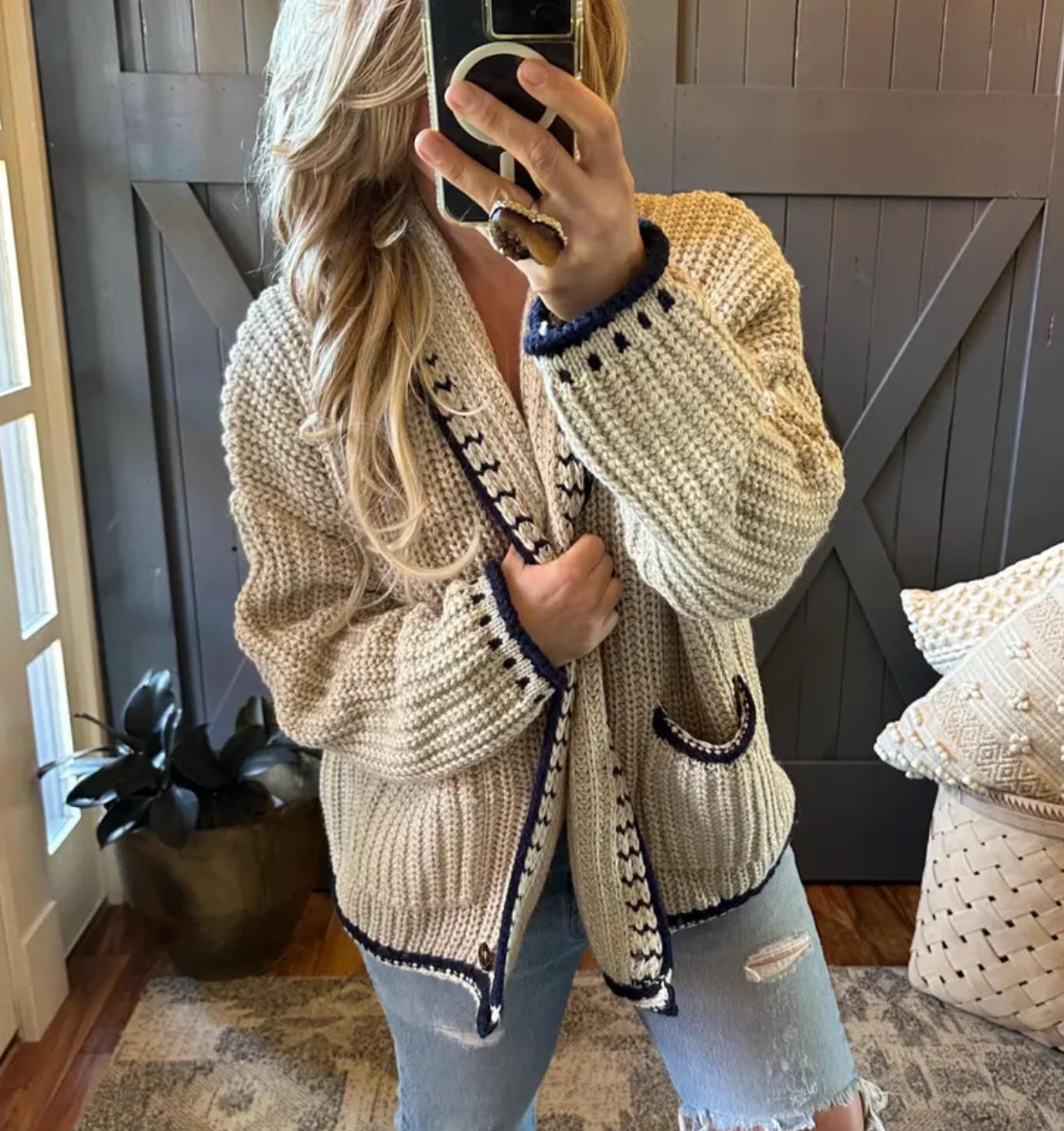 Person wearing a beige knitted cardigan with black accents in a home setting.