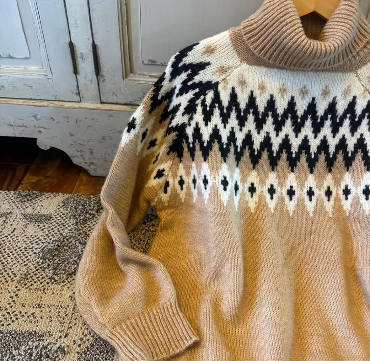 Beige sweater with black and white pattern draped over a wooden surface.