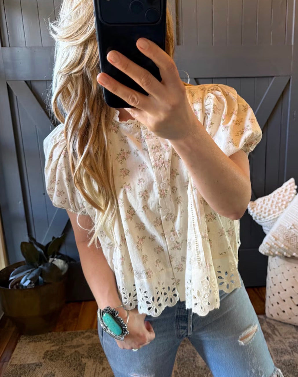 Person wearing a white lace top and blue jeans, taking a mirror selfie.