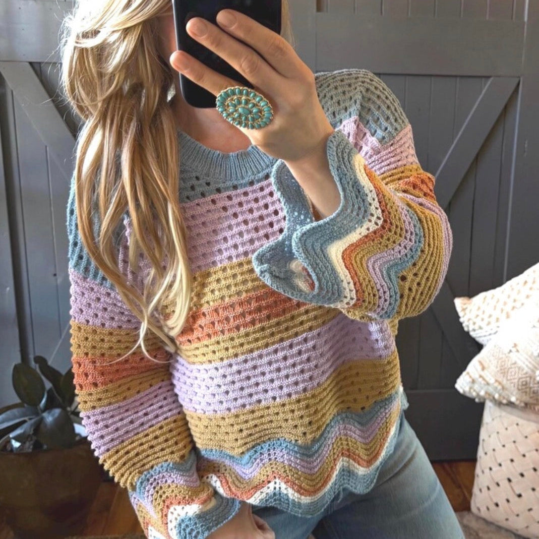 Person wearing a colorful crochet sweater taking a mirror selfie.
