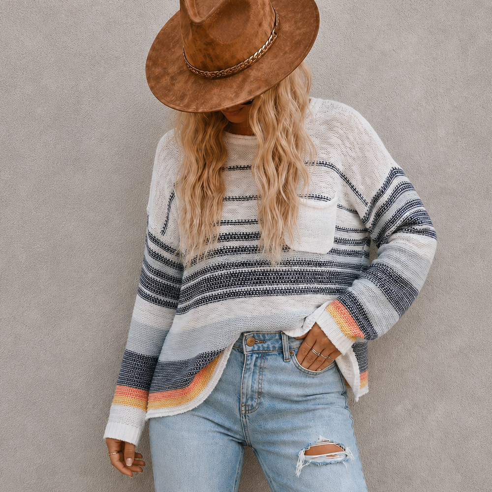 A woman wearing a brown wide-brim hat, a cream and navy striped knit sweater with orange stripes, and light blue ripped jeans, standing against a textured gray wall.