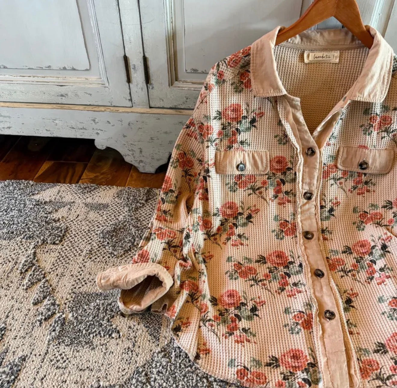 Floral patterned jacket with sherpa lining on a hanger against a rustic background