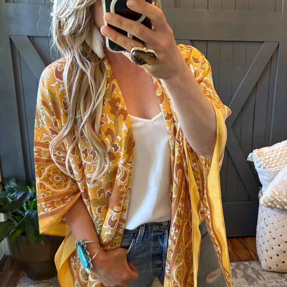 Person wearing a yellow patterned kimono over a white top and jeans, taking a mirror selfie.