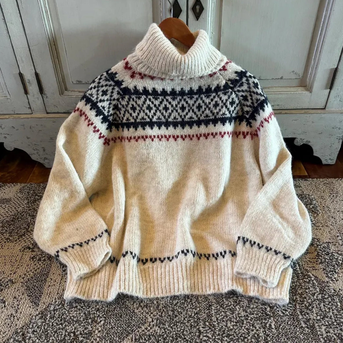 Beige sweater with patterned design on a wooden hanger against a neutral background