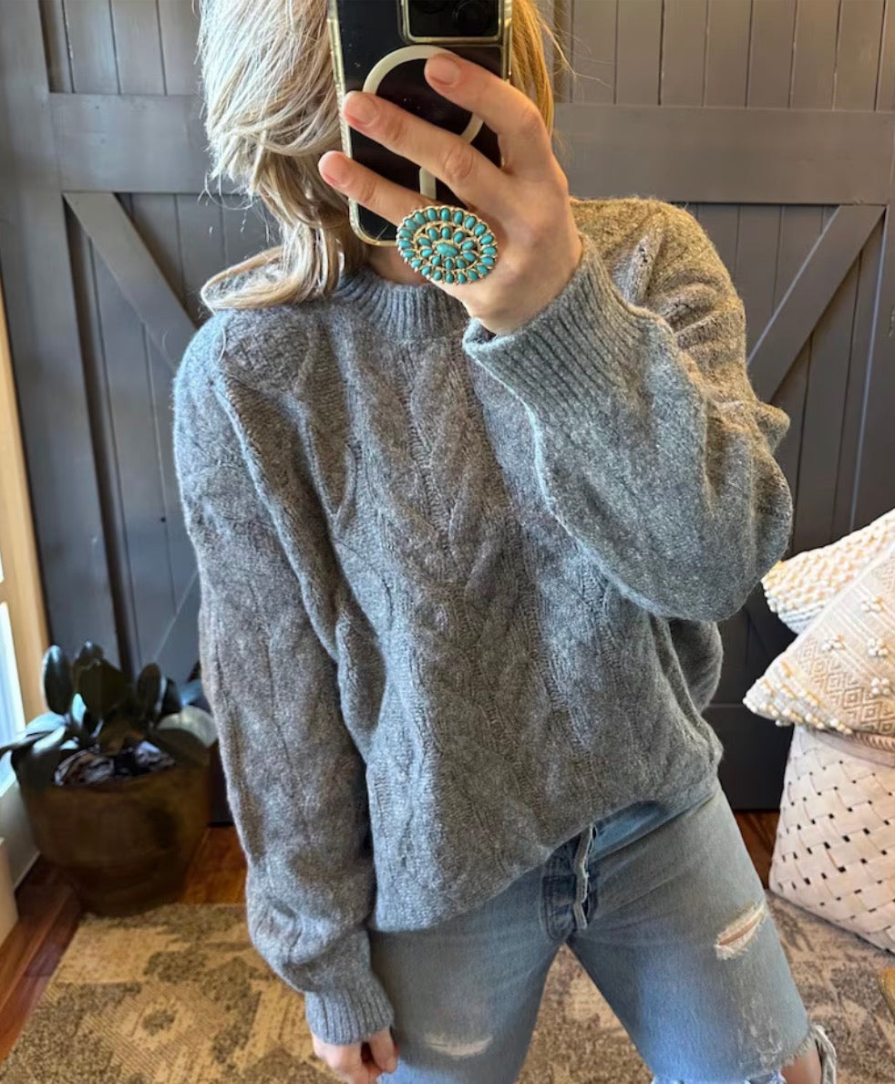 Person wearing a gray sweater and jeans, holding a phone with a decorative ring.