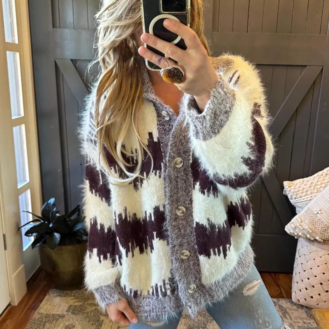 Person wearing a patterned cardigan taking a mirror selfie indoors.