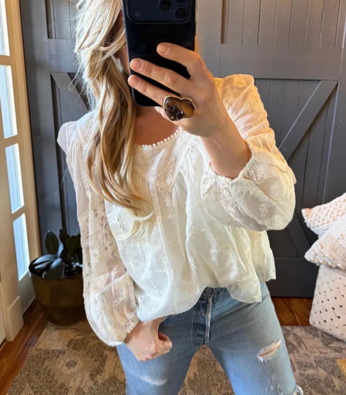 Person wearing a white lace top and blue jeans taking a mirror selfie.