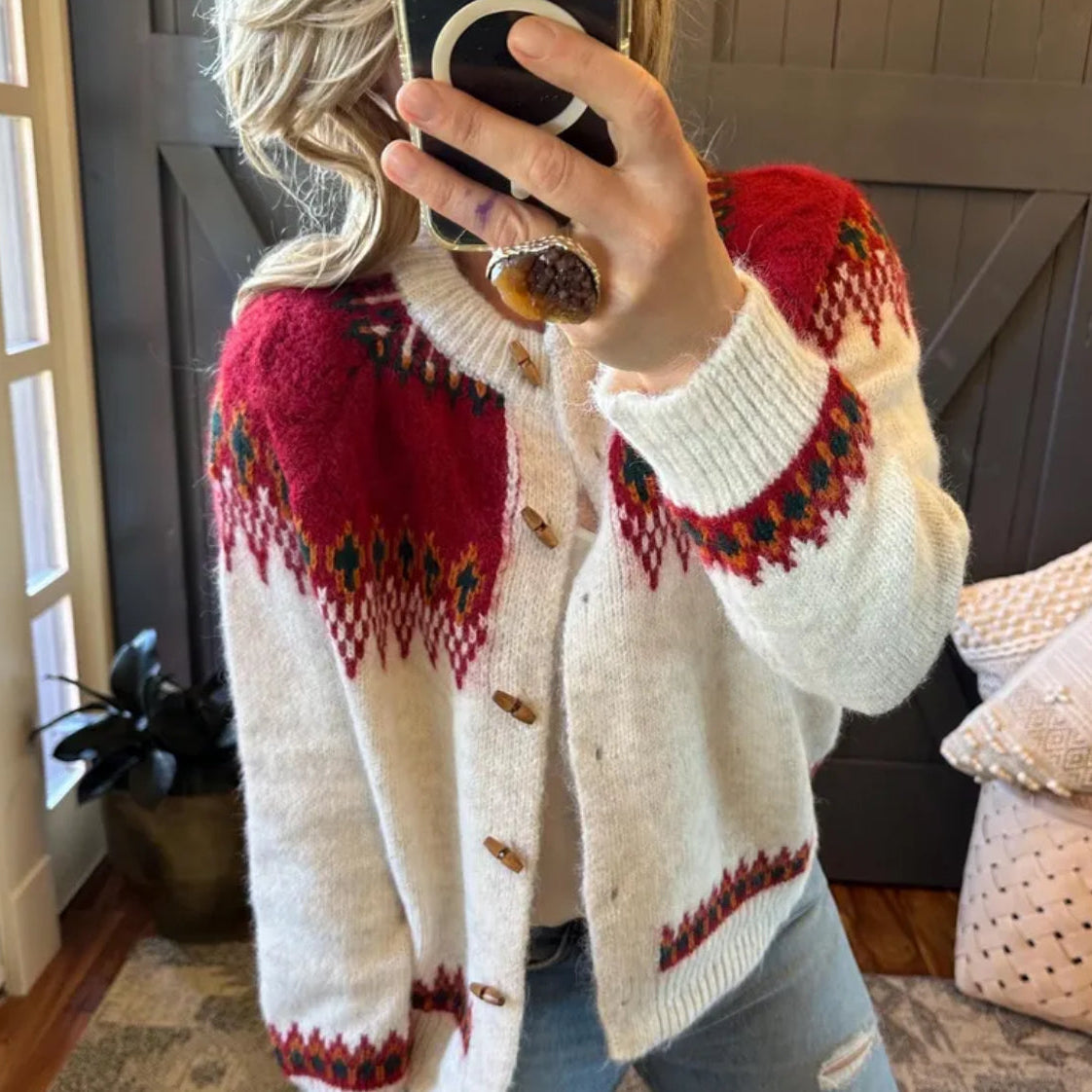 Person wearing a white cardigan with red and green pattern, taking a mirror selfie.