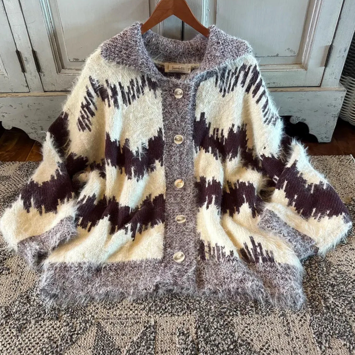 Cardigan with a pattern on a wooden hanger against a rustic background