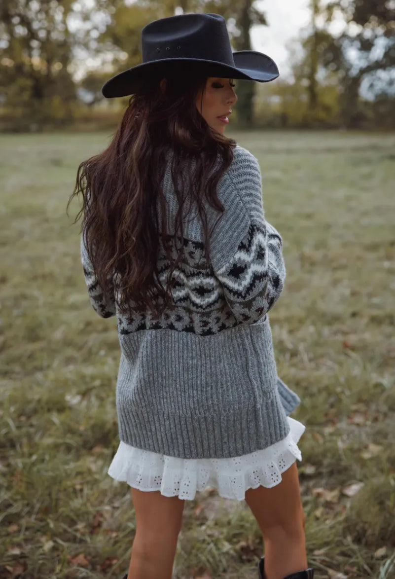 Woman wearing a gray patterned sweater and black hat in a field