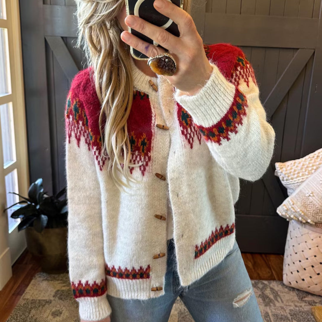 Person wearing a white sweater with red and black patterns, taking a mirror selfie.