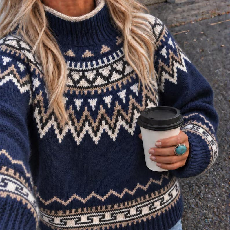 A woman wearing a navy blue knit sweater with a cream and beige Fair Isle pattern, holding a white coffee cup with a black lid.