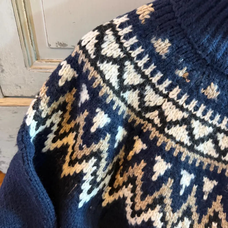 Close-up of a knitted sweater with a dark navy base and a Fair Isle style pattern in cream, tan, and light blue.
