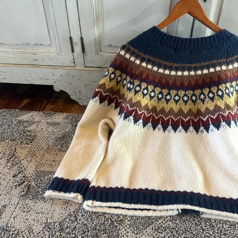 Knitted sweater with a pattern on a hanger against a wooden cabinet background