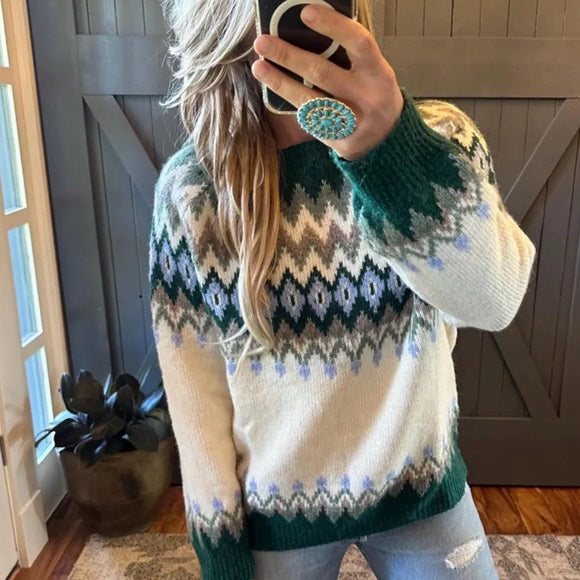Person wearing a patterned sweater taking a mirror selfie indoors.