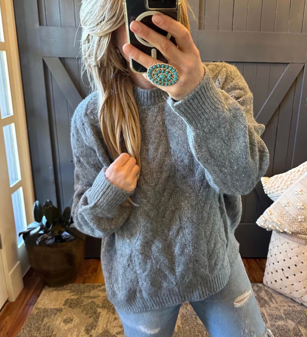 Person wearing a gray sweater taking a mirror selfie in a home setting.