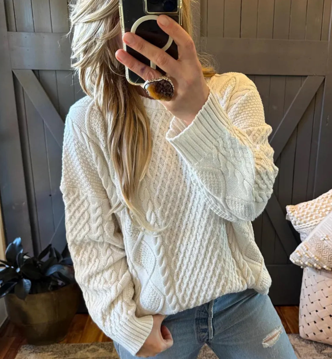 Person wearing a white cable knit sweater taking a mirror selfie.